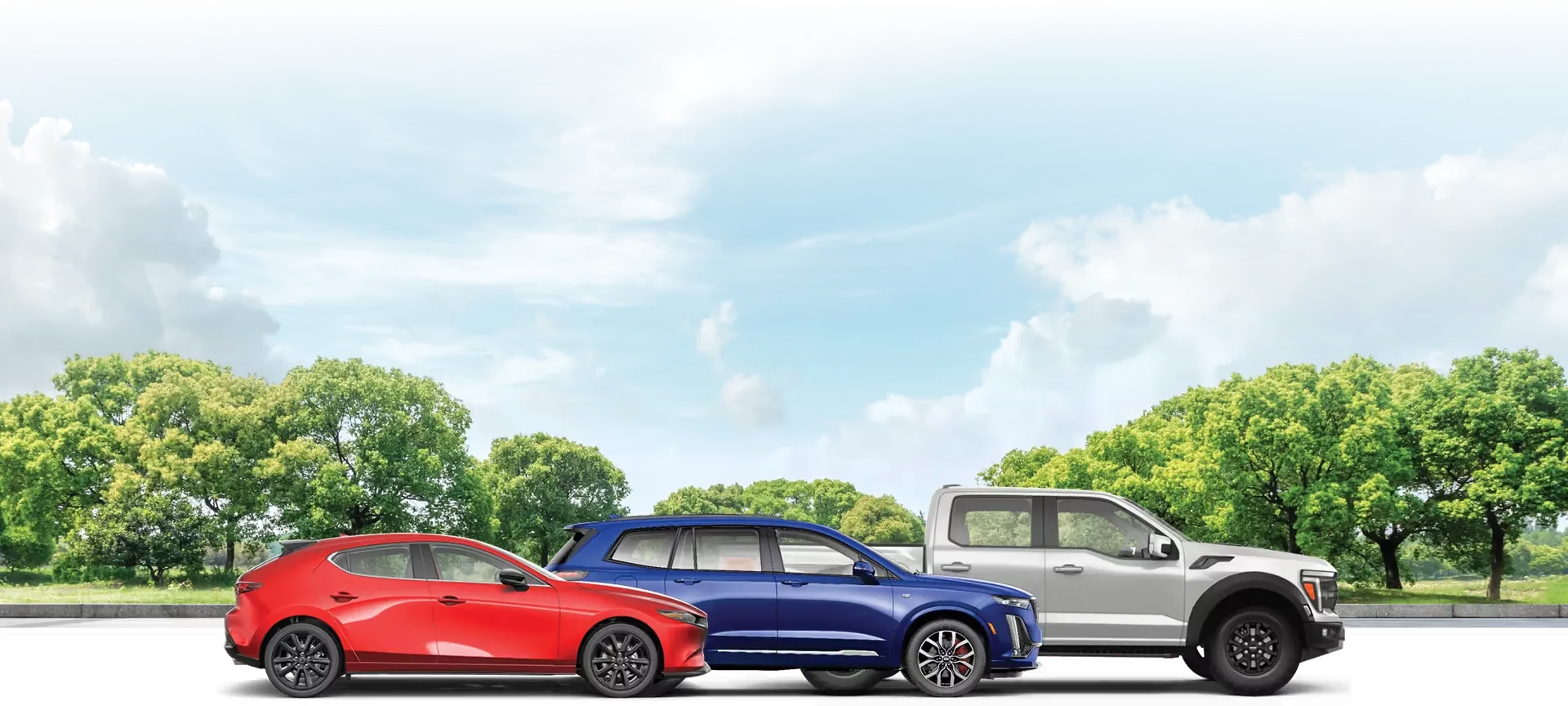 Mazda, Ford and GM vehicles in front of blue sky and trees.