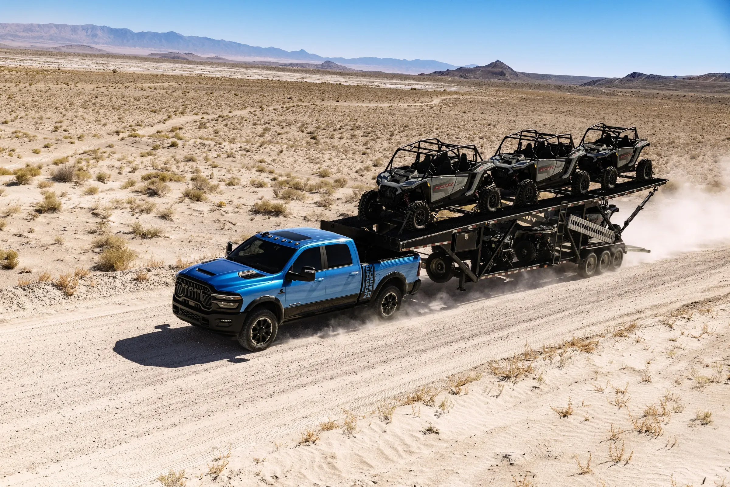 Blue Ram Power Wagon towing a trailer loaded with three UTVs across the desert