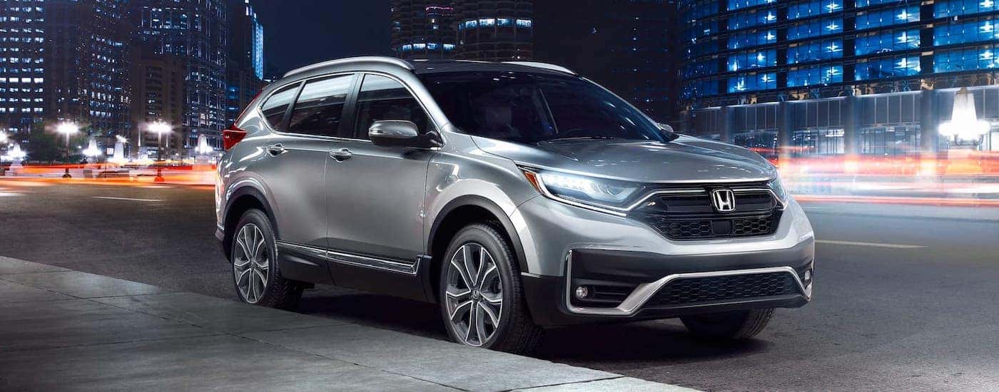 A silver 2020 Honda CR-V on a lit up city street at night.