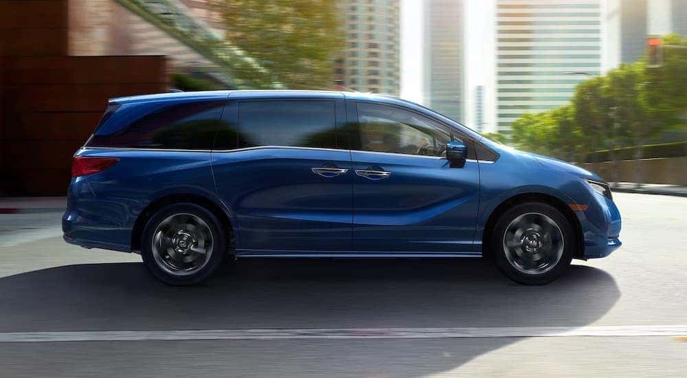 A blue 2024 Honda Odyssey is shown from the side on a city street.