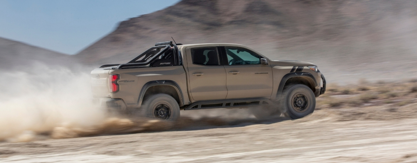 A tan 2023 Chevy Colorado ZR2 Desert Boss is shown kicking up dust off-road.