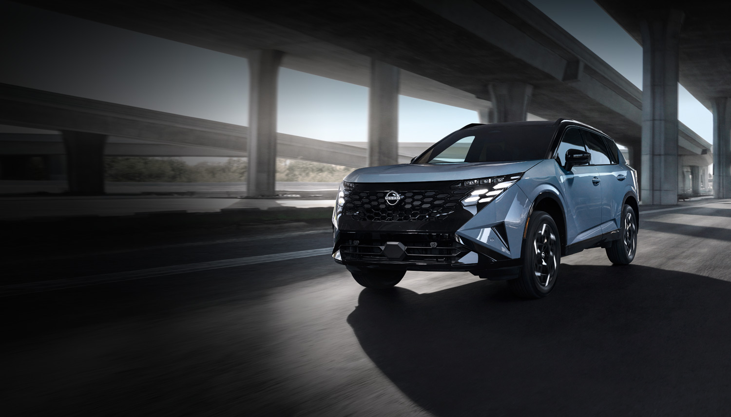 Light blue two-tone 2027 Nissan Rogue Hybrid SUV with a black roof driving under a concrete highway overpass at dusk, shown from a front three-quarter angle with motion-blurred surroundings.