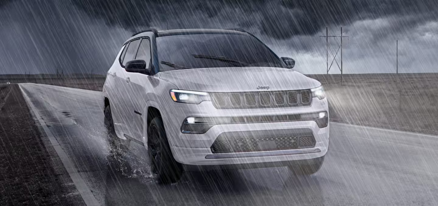 A white jeep driving in the rain.