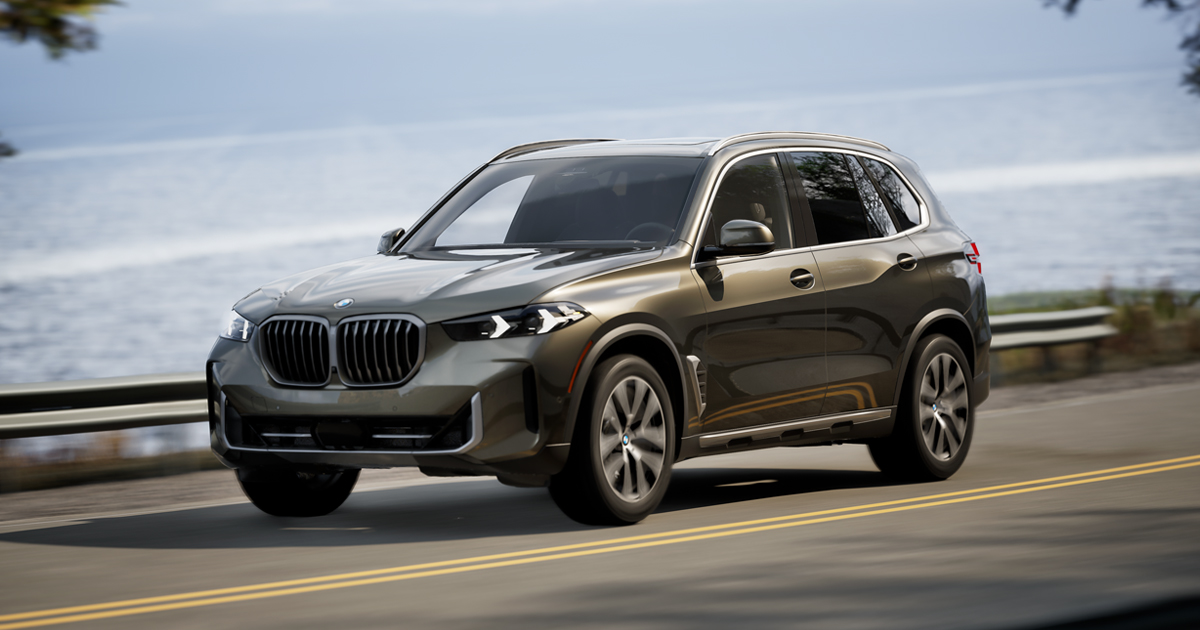 A silver BMW X5 driving on an oceanside road.