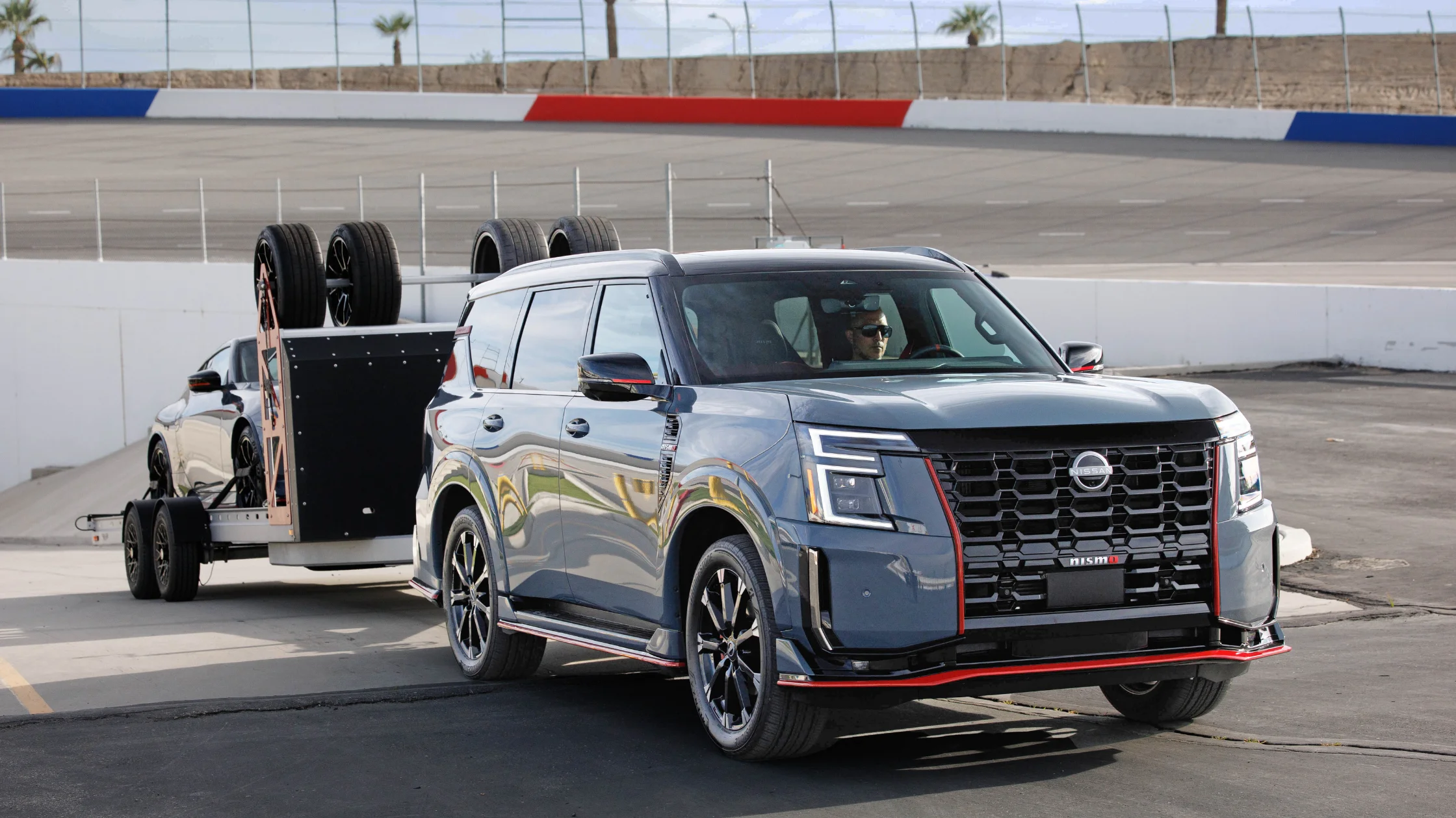 2026 Nissan Armada® towing track trailer near speedway with bold grille and NISMO red accents
