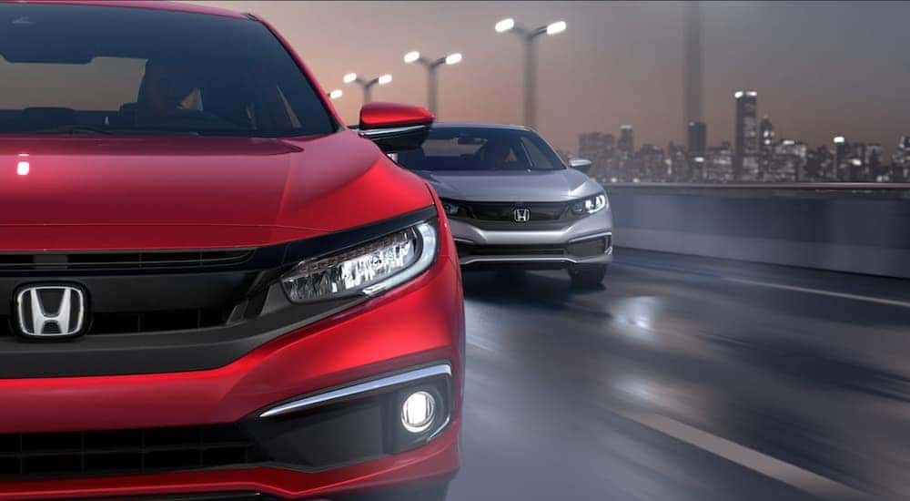A red and a silver 2016 Honda Civic LX are shown driving on a wet road at night.