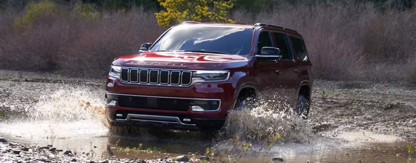 A maroon 2023 Jeep Wagoneer is shown splashing through a creek.