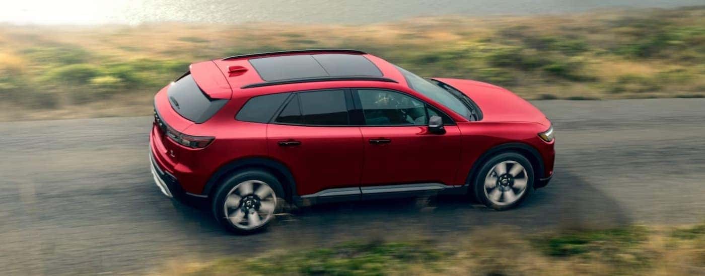 A red 2025 Honda Prologue Elite driving on a backroad.