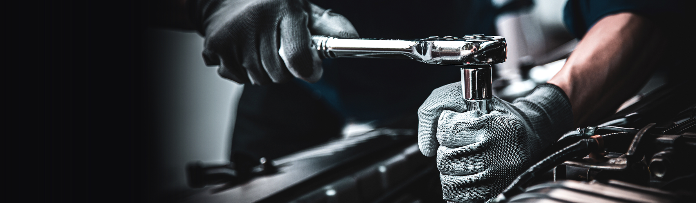 A mechanic tightens a bolt under the hood of a car