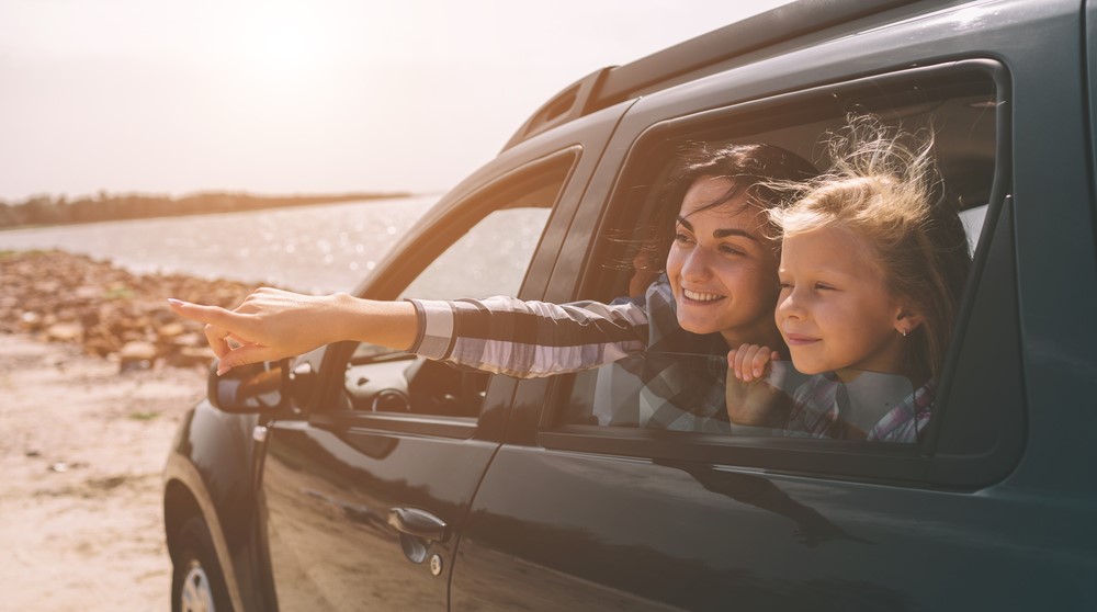 Mother points to direct young daughter's gaze as they look out the window from inside their vehicle parked on a beach