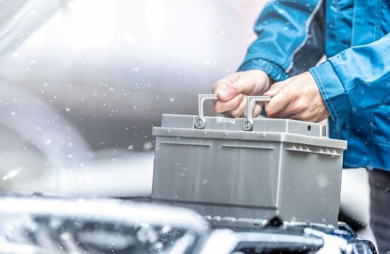 A person holding a car battery surrounded by snowfall