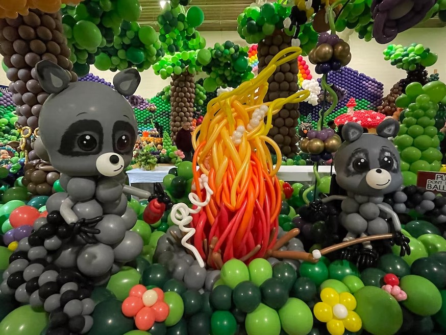 two raccoons made from balloons sitting near a fire, also made of balloons