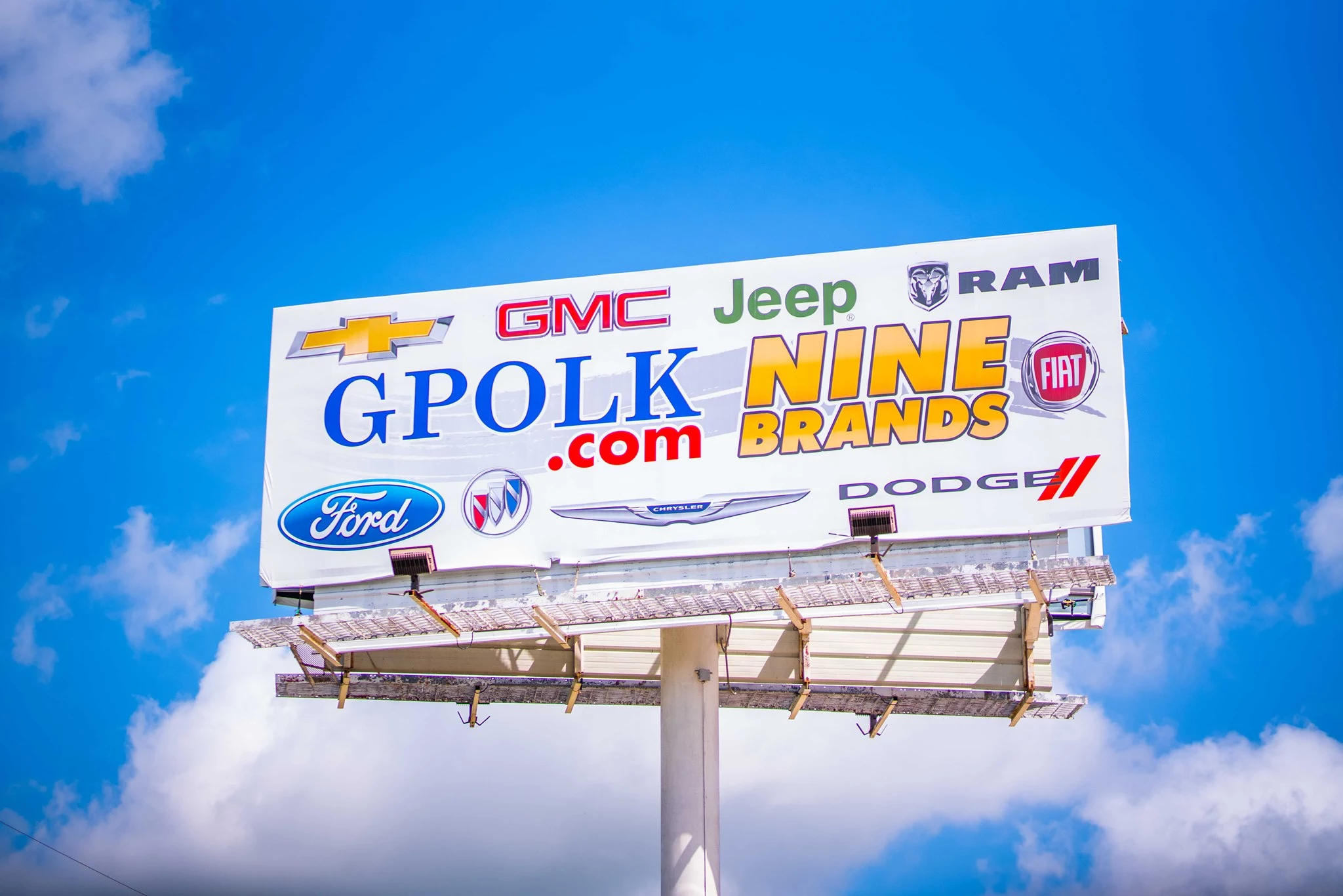 A billboard cast against a blue sky with the Glenn Polk logo, text that says 'Nine Brands', and then the logos of each brand scattered across the billboard.