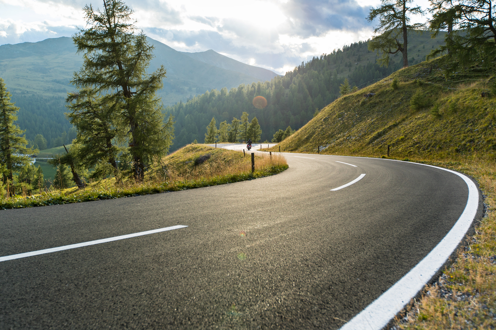 open road going around a corner, pine trees and mountain landscape