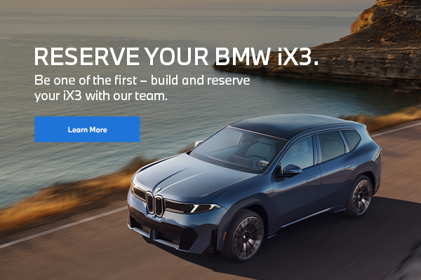 BMW iX3 vehicle driving on a road near mountains and water.