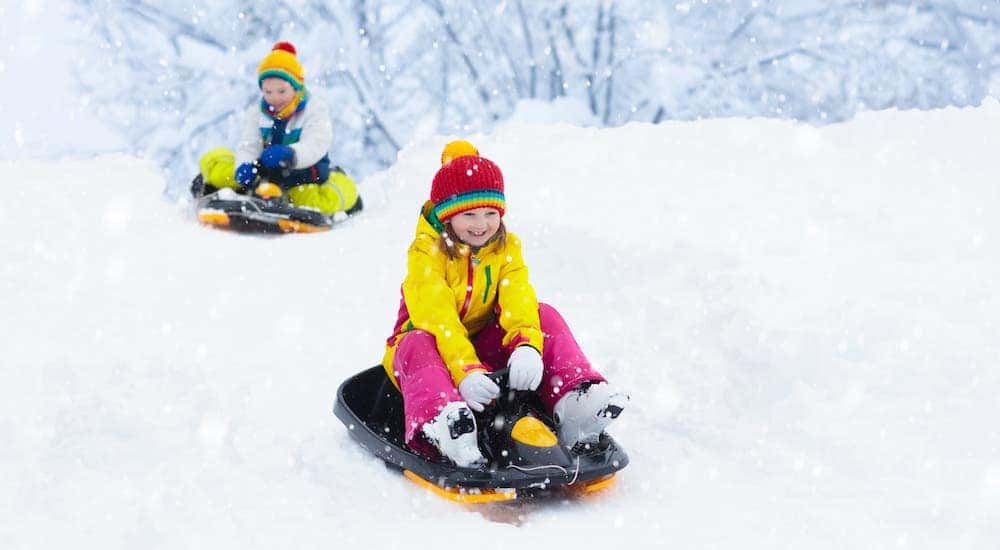 Two children are sledding in the snow.