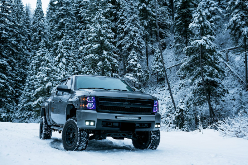 Grey pickup truck on snow field surrounded by trees.