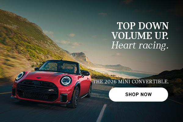 Red MINI convertible driving along a coastal road with mountains and ocean in the background, with advertisement text promoting the 2026 Mini Convertible and a “Shop Now” button.