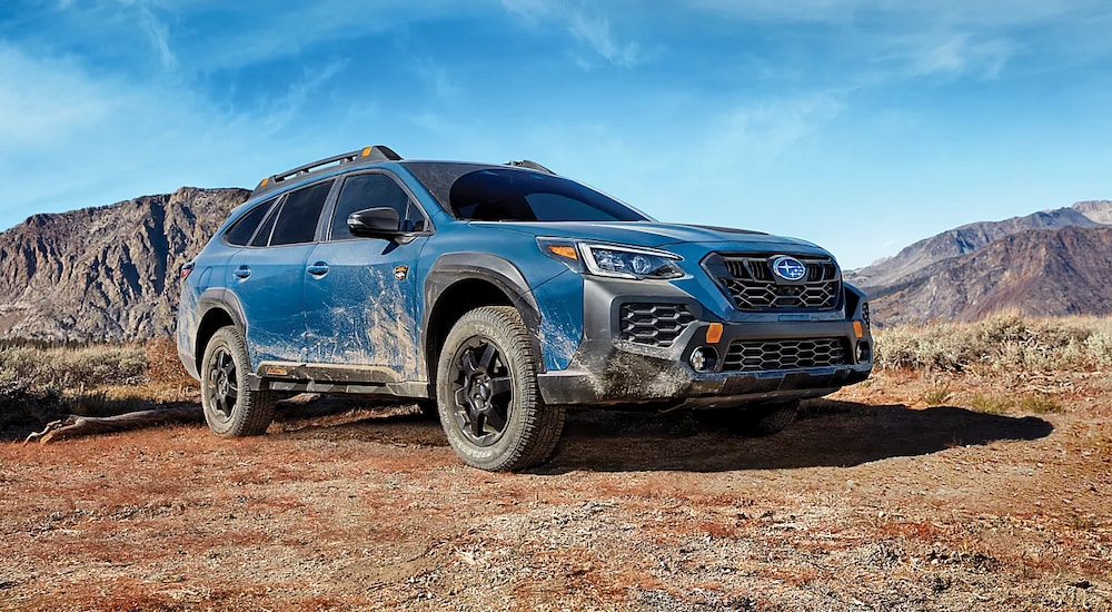 A blue 2025 Subaru Outback Wilderness muddy and parked in the mountains.