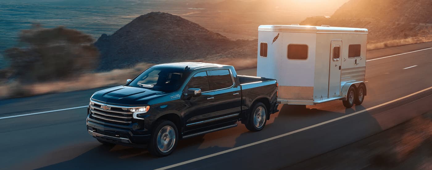 A black 2022 Chevy Silverado 1500 High Country is towing a small enclosed on an open highway.