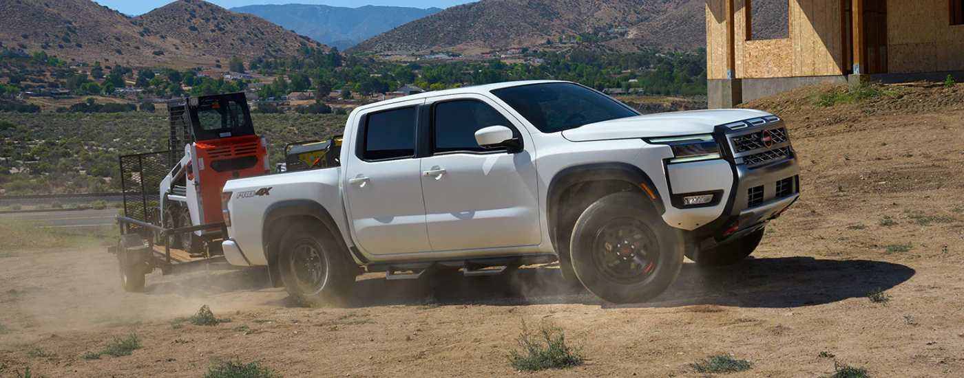 White 2026 Nissan Frontier PRO 4x towing a bobcat