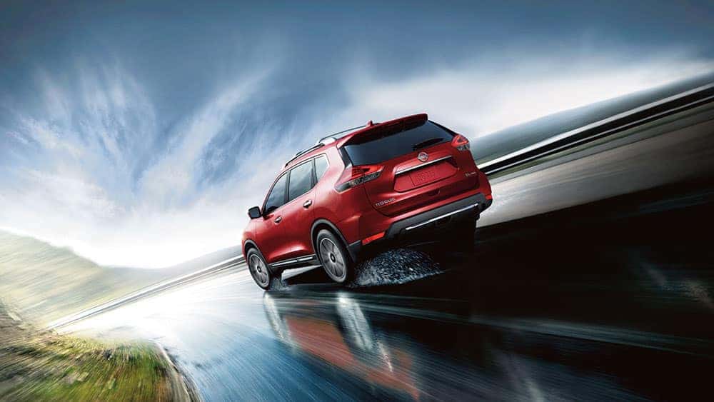 Red 2017 Nissan Rogue driving on a coastal road, rear three-quarter view
