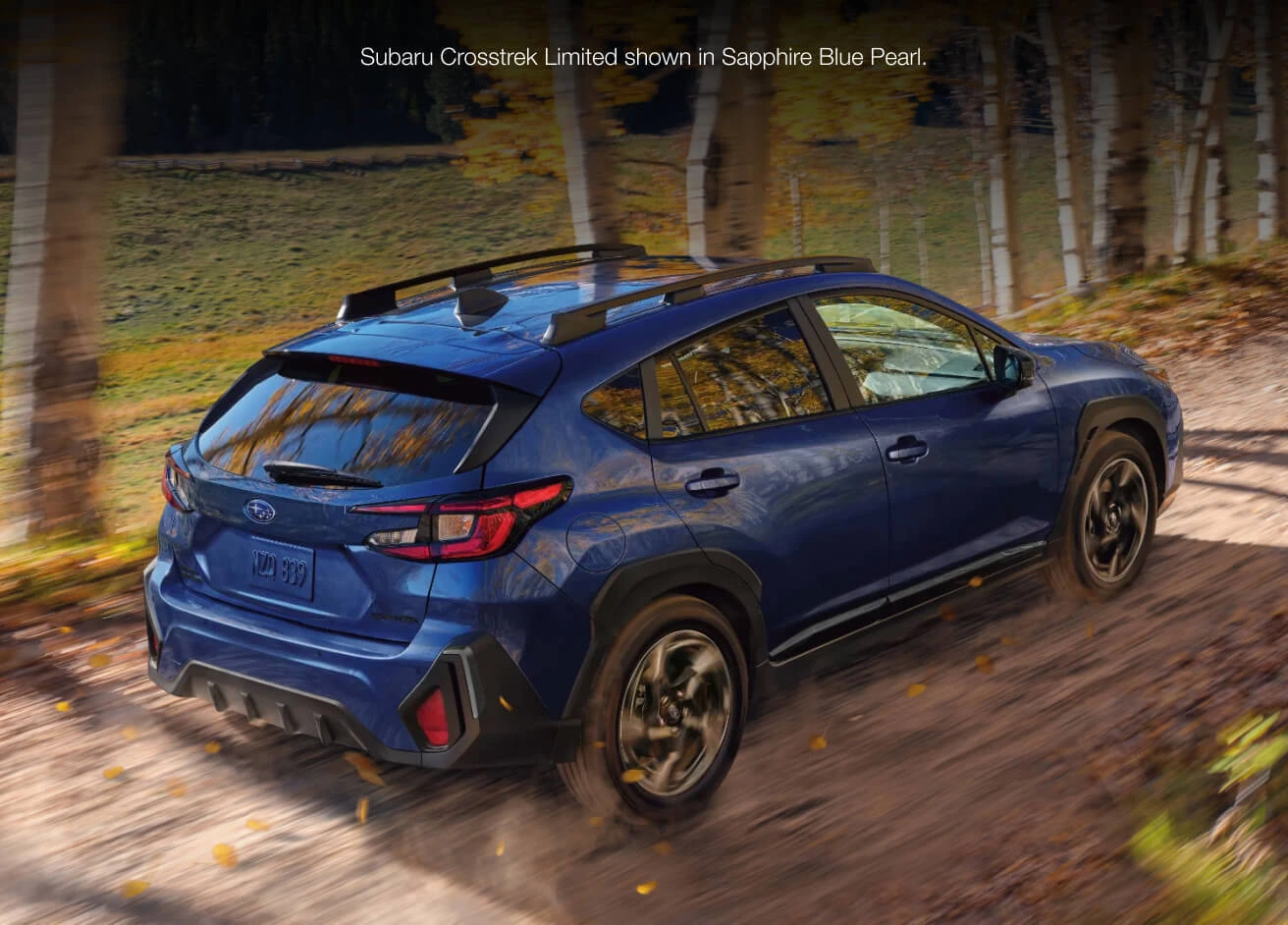 Sapphire Blue Pearl Subaru Crosstrek Limited driving along a dirt path scattered with autumn leaves.
