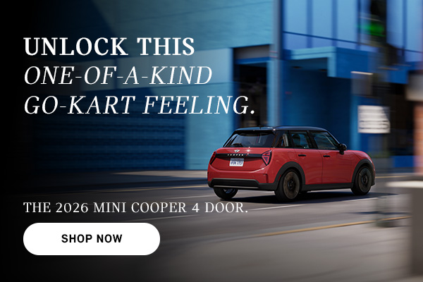Red MINI Cooper 4-door driving on a city street, with motion blur in the background and ad text promoting the 2026 model and a “Shop Now” button.