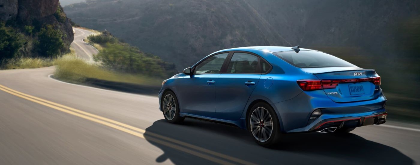 Blue 2023 Kia Forte GT driving on a winding road