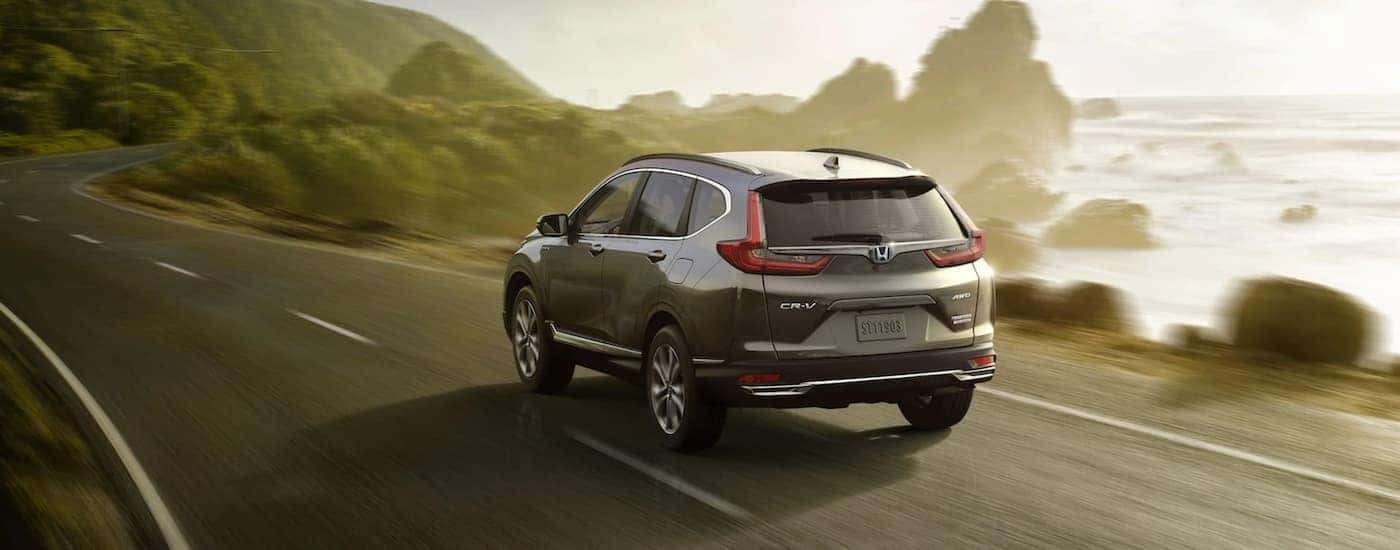 A gray 2021 Honda CR-V is shown from the rear driving down an empty road past a body of water.