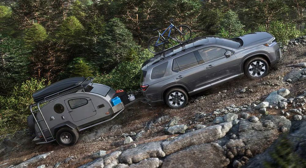 Grey 2026 Honda Pilot towing a pop-up camper off-road.