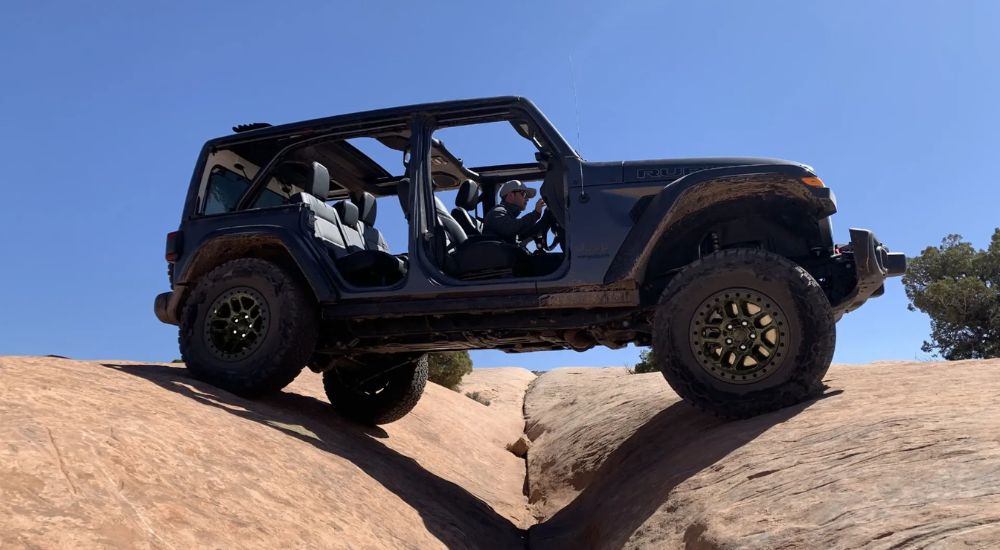 A grey 2024 Jeep Wrangler Rubicon is shown from the side while crawling over rocks.