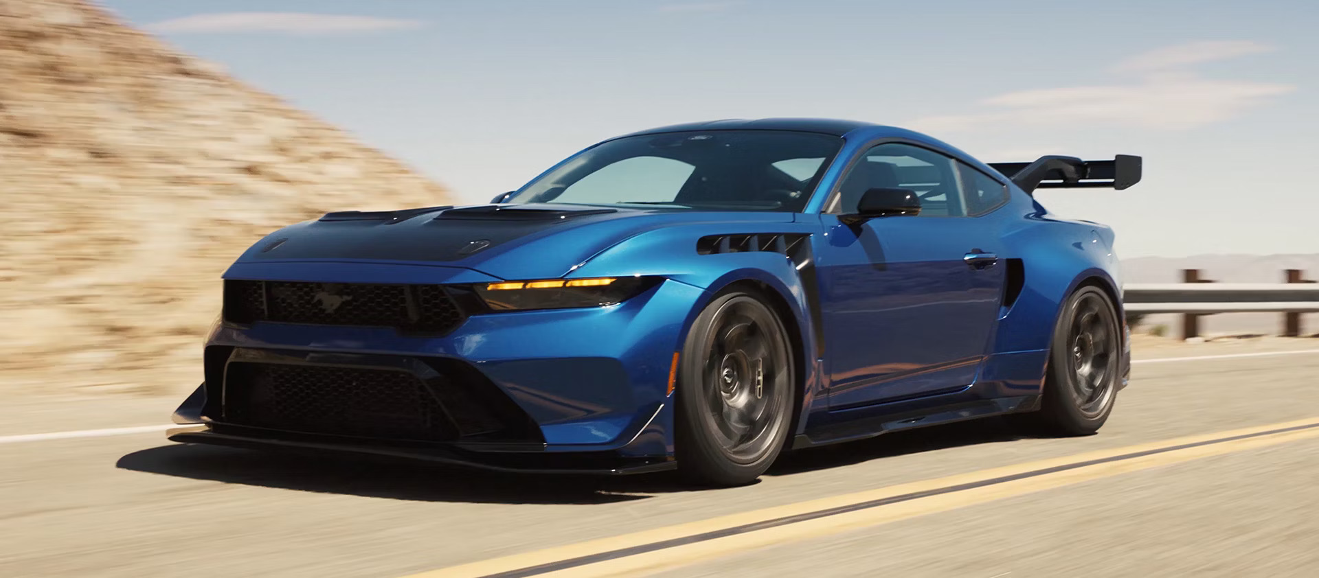 2027 Ford Mustang GTD in blue driving on a desert mountain road, front three-quarter view
