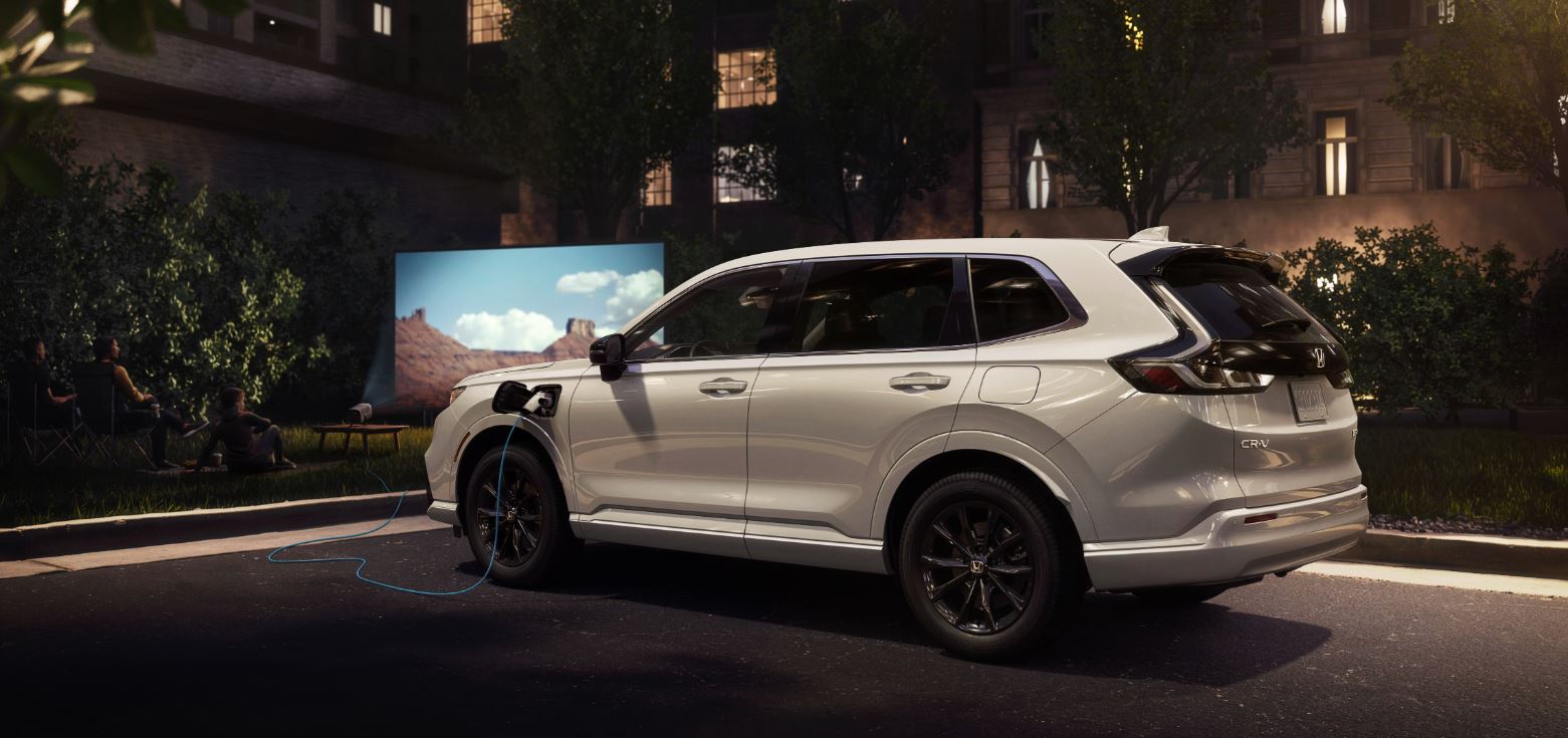 white 2025 Honda CR-V e:FCEV plugged into a charging station while family watches a movie on projector screen