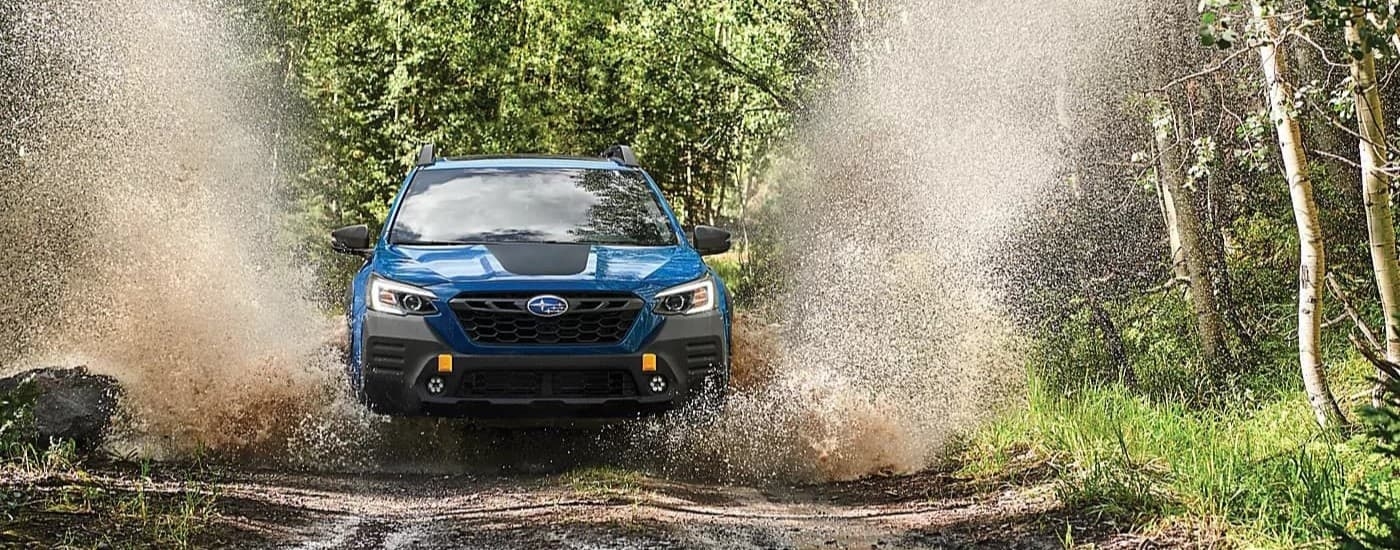 Blue 2024 Subaru Outback Wilderness driving over a muddy puddle