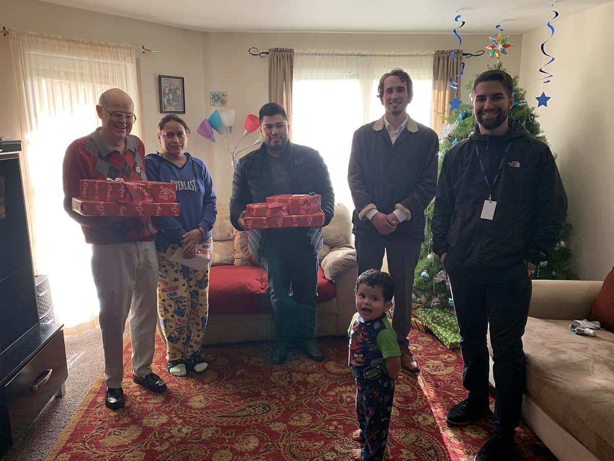 Volunteers holding wrapped gifts in a family's living room