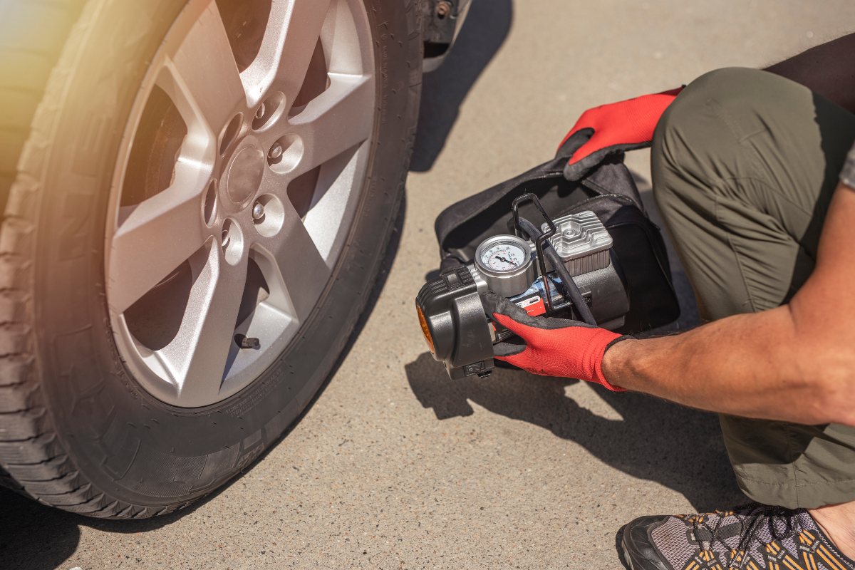 Man Holding Portable Air Compressor near Tire