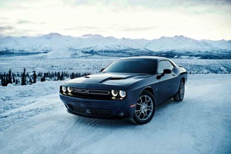 Dark gray Dodge Challenger driving on a snowy road with mountains behind