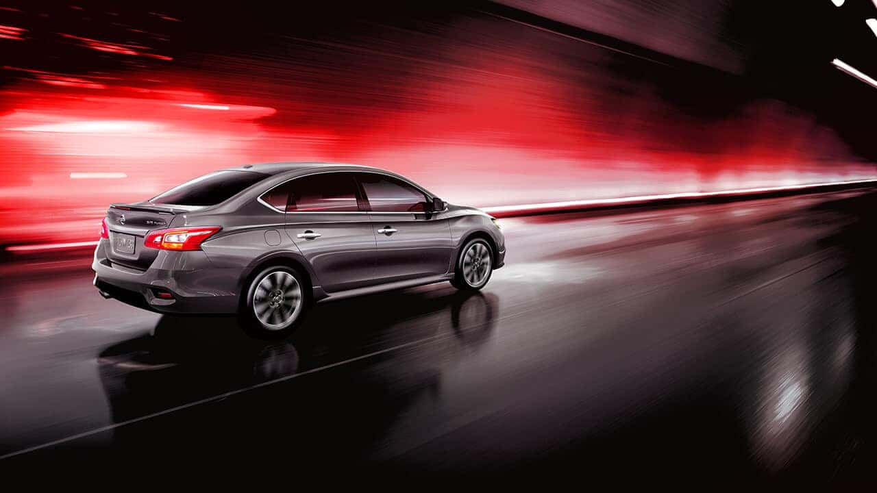 Gray 2017 Nissan Sentra sedan driving past a red-lit wall