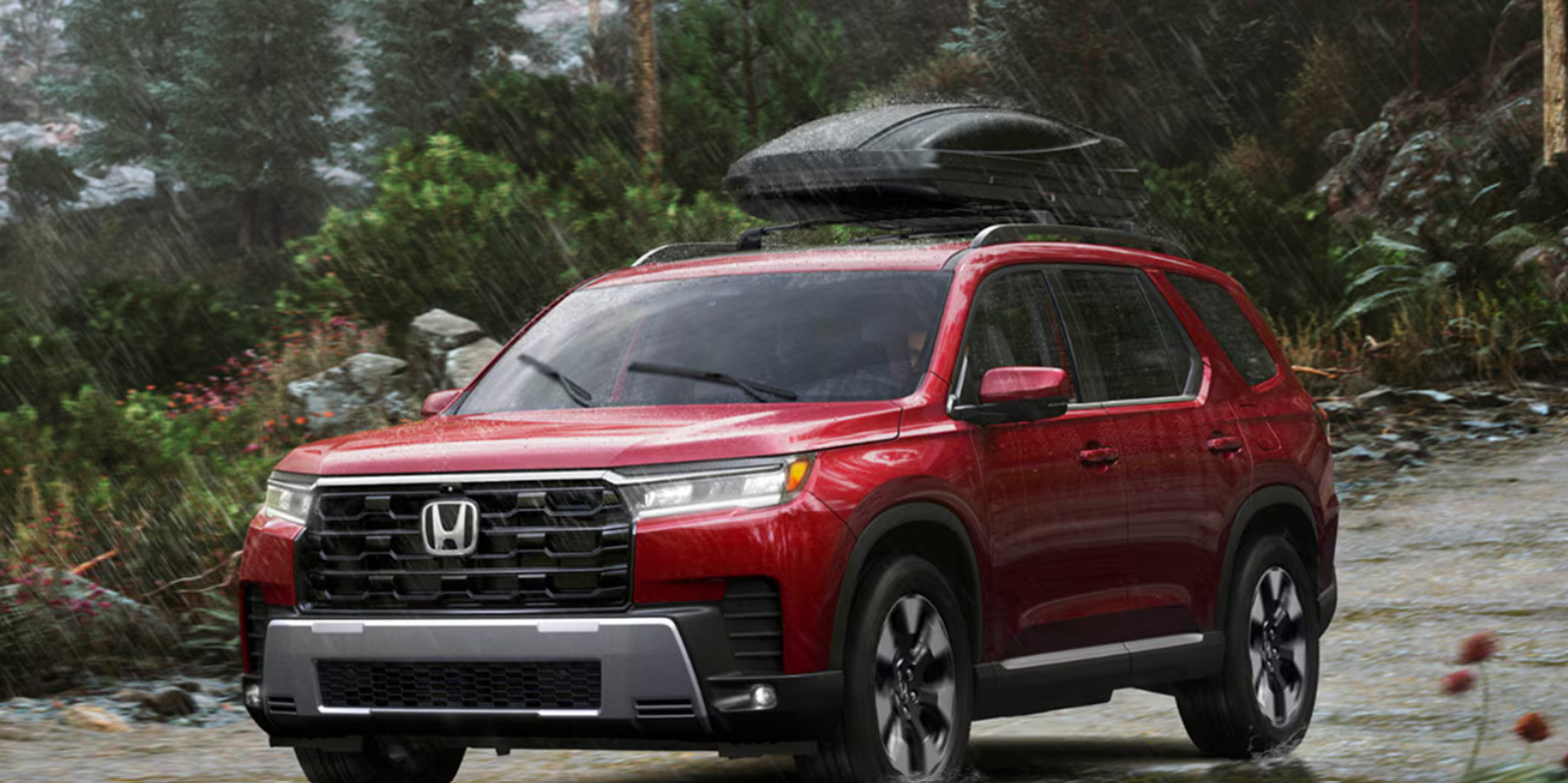 The red, new 2026 Honda Pilot drives through rain in a mountainous terrain.