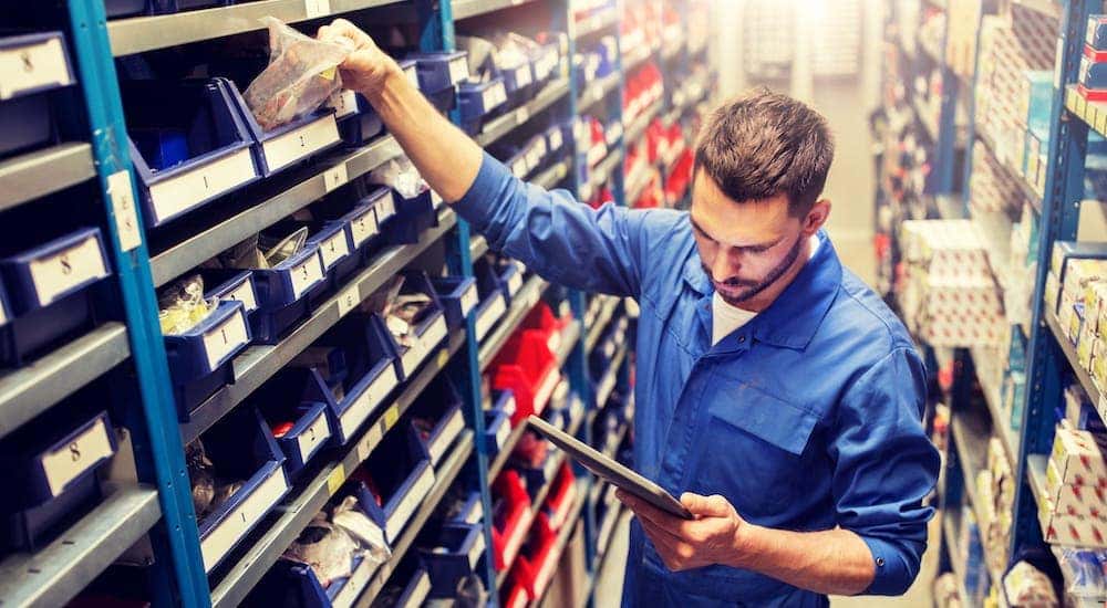 A mechanic in a blue jump suit picking out parts in a warehouse.