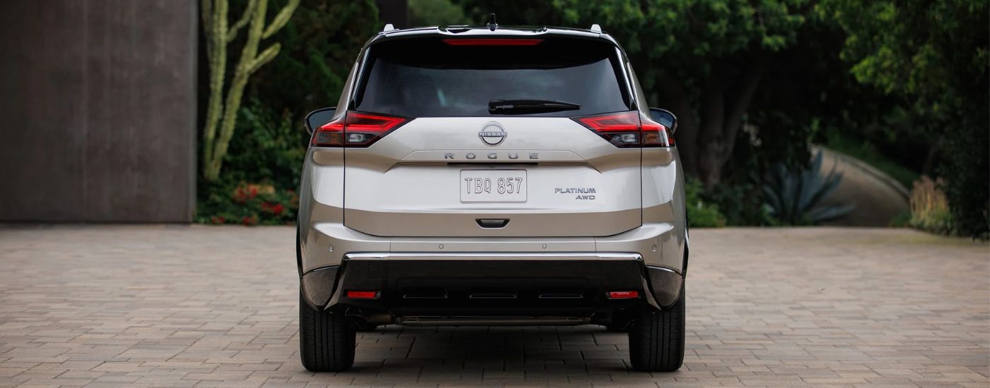 Rear view of a tan 2026 Nissan Rogue Platinum parked in a driveway.