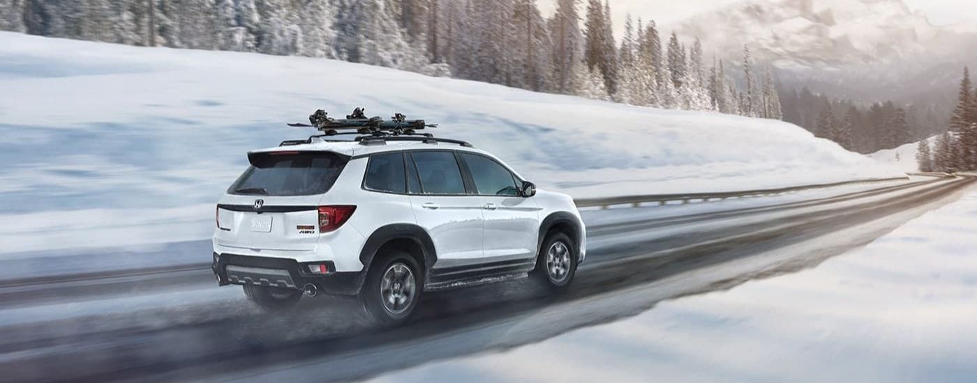 White 2023 Honda Passport TrailSport driving on a snowy highway