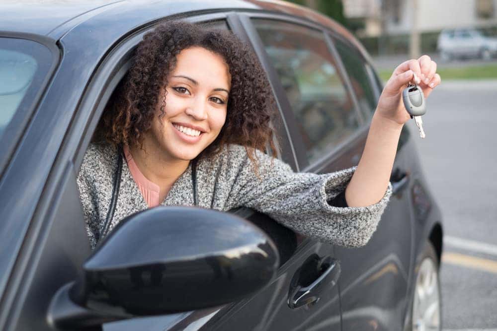 A woman is holding car keys outside of her vehicle window.