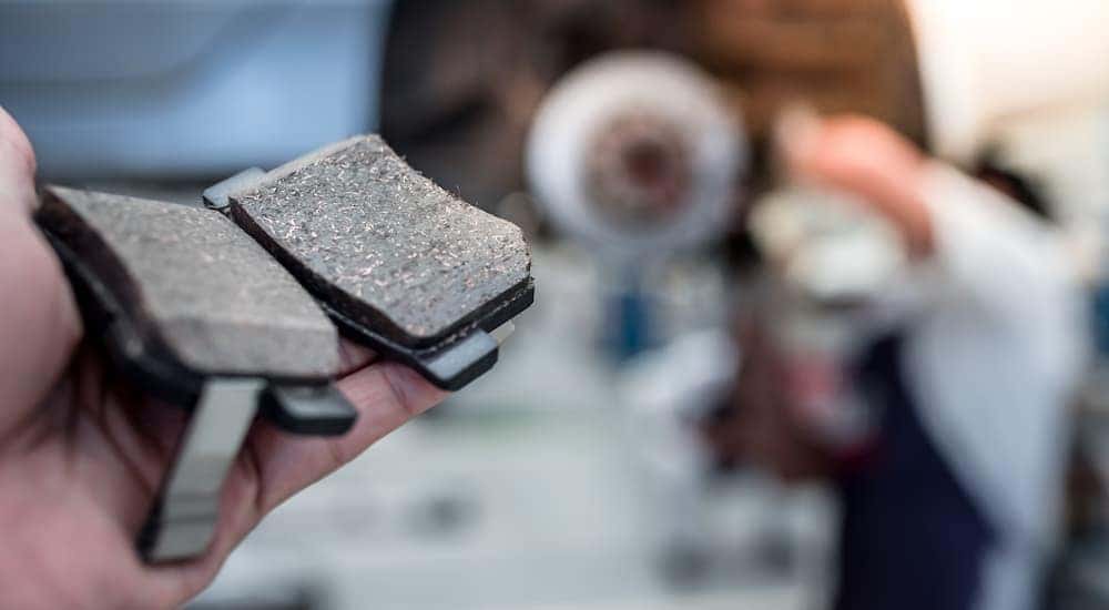A mechanic is holding brake pads while performing a Brake service near Greece.