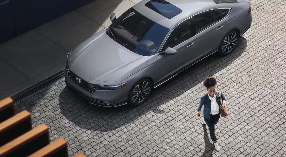 A woman is walking away from a grey 2025 Honda Accord Touring Hybrid.