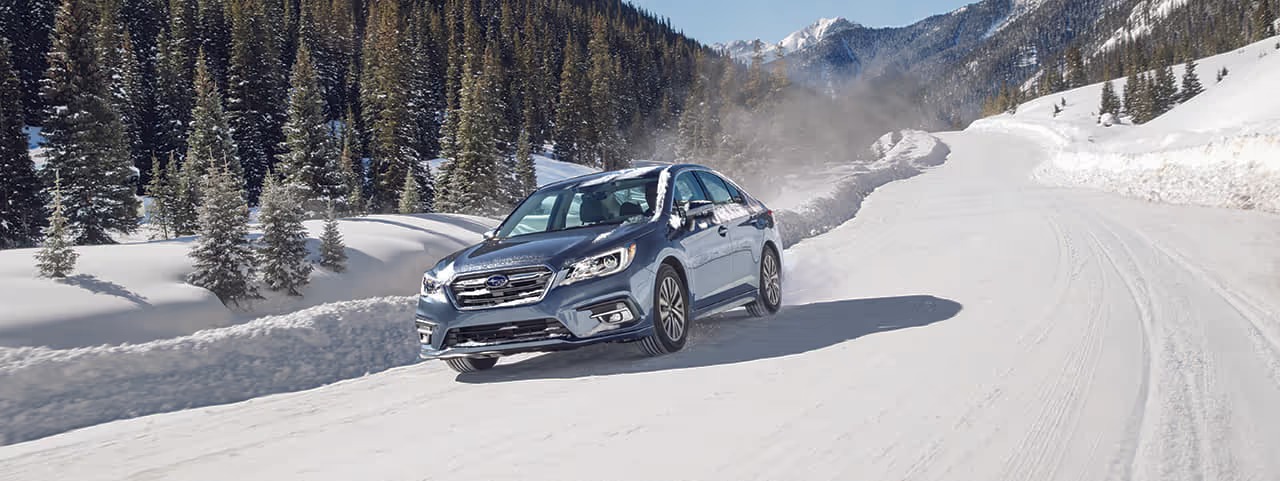 Subaru Legacy sedan driving on a snowy mountain road