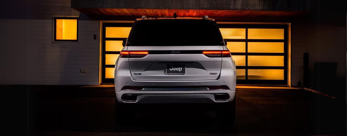 The rear of a white 2024 Jeep Grand Cherokee Summit Reserve 4xe parked in a driveway in front of a garage.