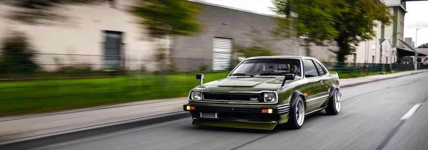 Forest green 1979 Honda Prelude speeding down a street