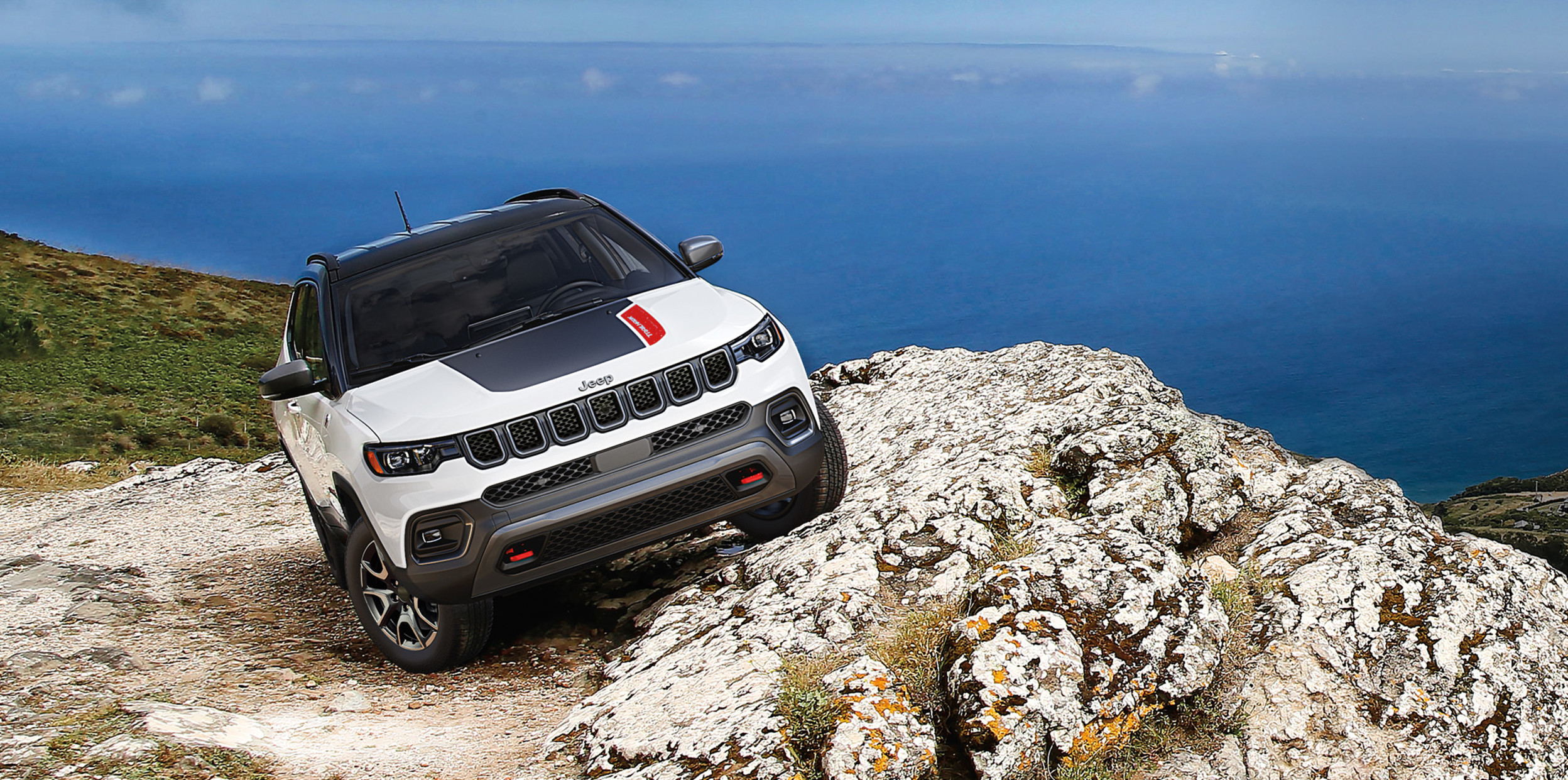 2024 Jeep Compass Trailhawk in white climbing rugged rocks, demonstrating its superior off-road capability with Jeep Active Drive Low 4x4 system